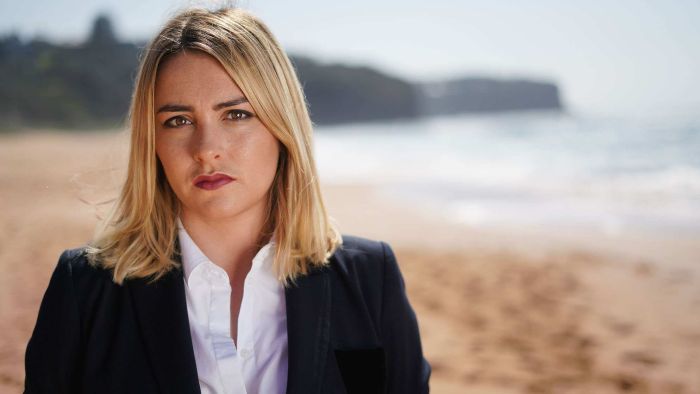 A woman in a blazer stands on a beach